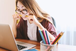 woman at her laptop biting a pencil out of stress
